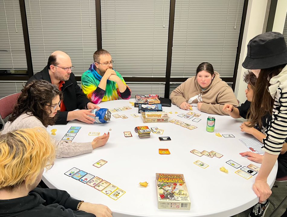 Engaged group enjoying game night, hosted by FAHASS' Pride Center FXBG in Fredericksburg, VA, with participants focused on game in the center of the table.