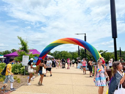 A photo of a rainbow archway with various Pride attendees walking around, showing the entrance to Riverfront Park, where Fredericksburg Pride was hosted this year by FAHASS, Pride Center FXBG, and Fredericksburg Pride.