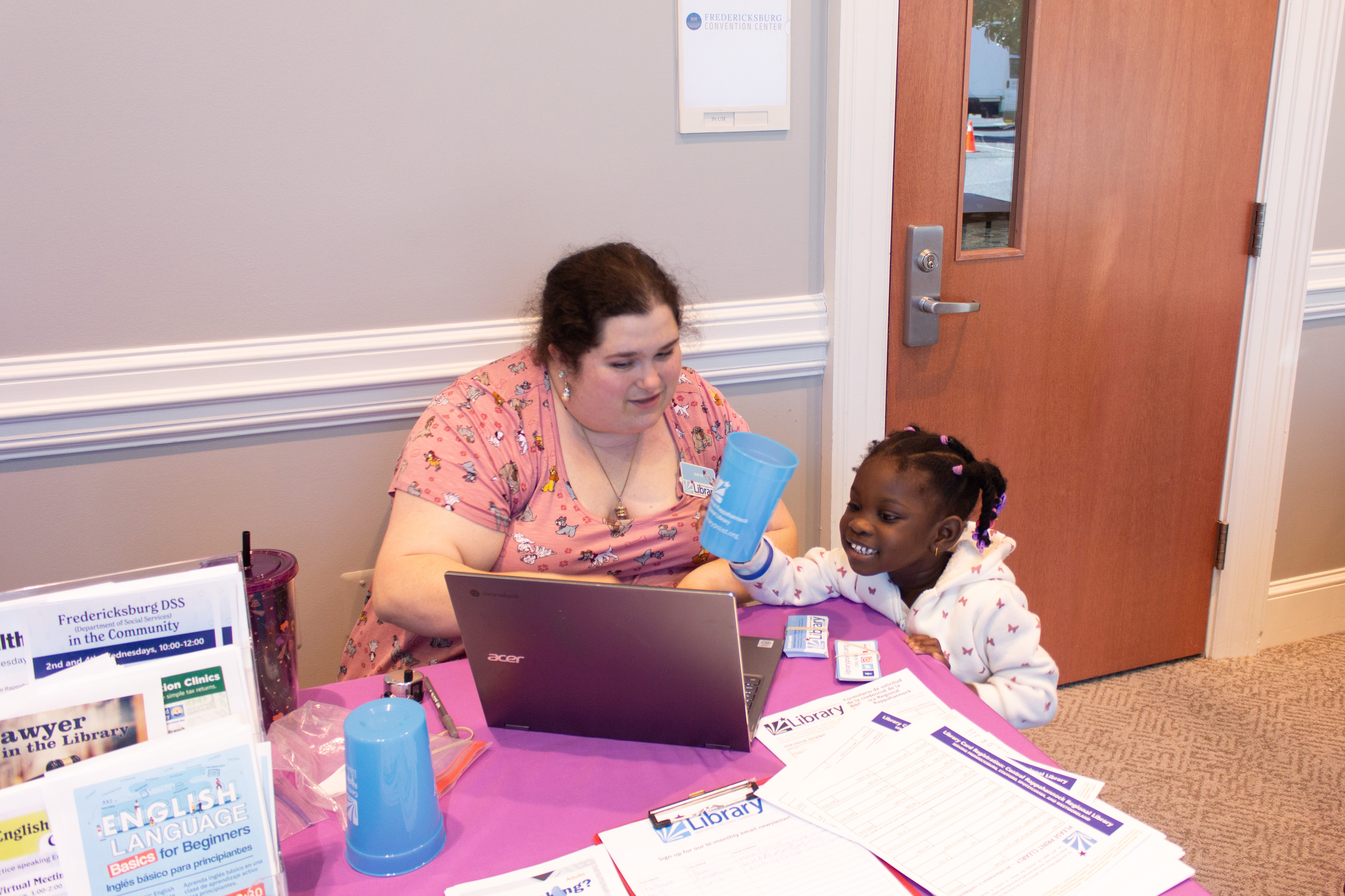 At a Community Connections Expo in Fredericksburg, VA, a woman and a young girl are engaged in a cheerful interaction at an information booth.