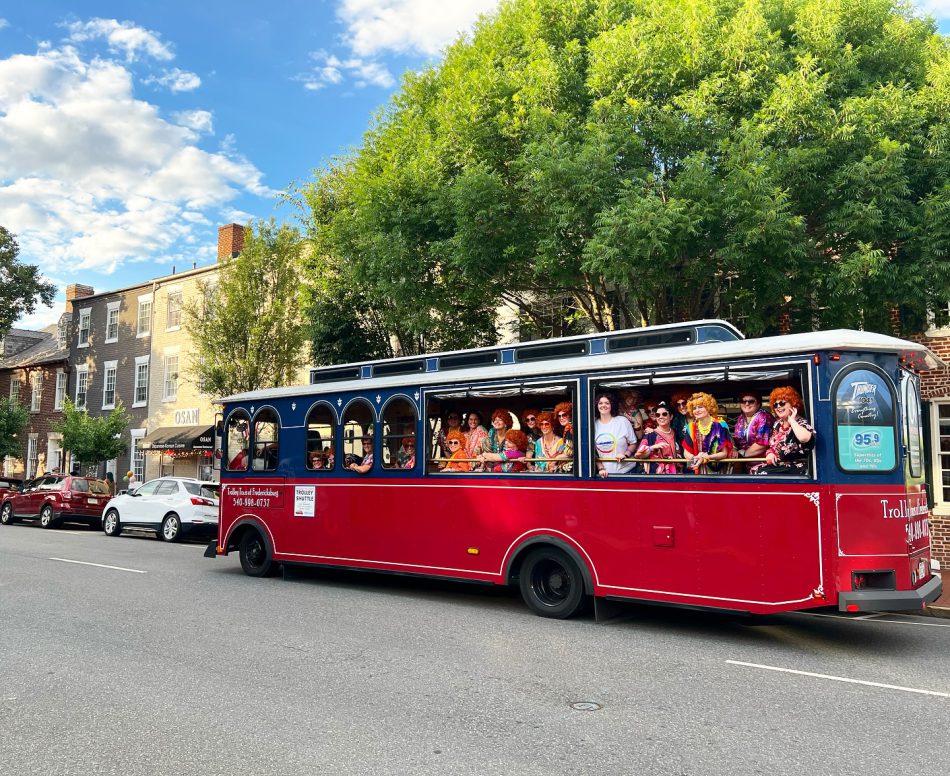 Group photo of diverse people on a trolley dressed up for a Mrs. Roper Romp hosted by FAHASS and the Downtown Dolls in Fredericksburg, VA.