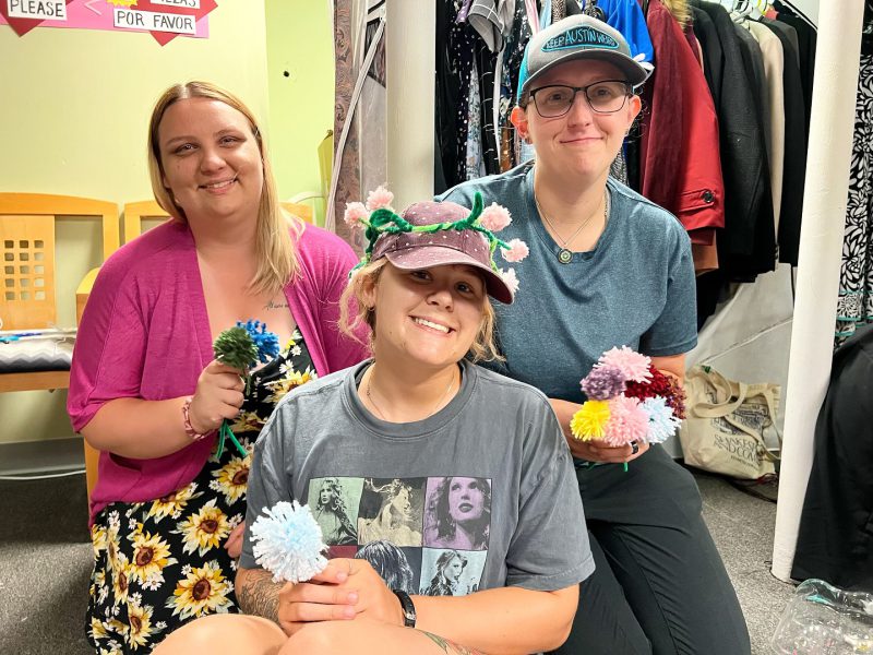 Three diverse friends showing off the flower crowns they made at Queer Craft Night hosted by Pride Center FXBG in Fredericksburg, VA.