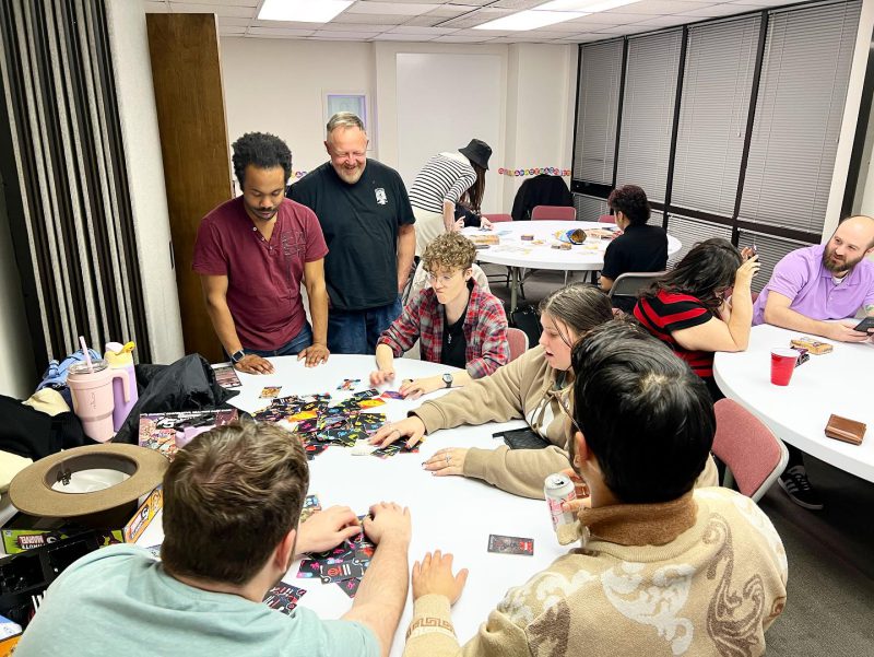 Engaged group enjoying game night, hosted by FAHASS' Pride Center FXBG in Fredericksburg, VA, with participants focused on game in the center of the table.