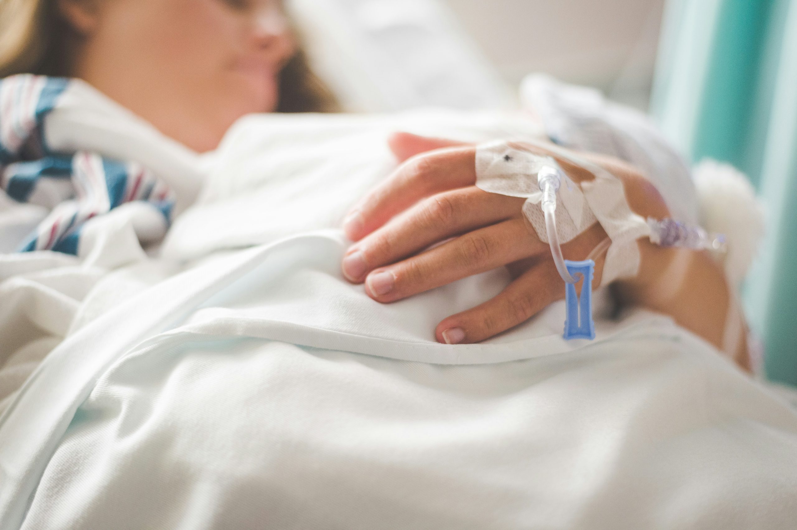 A close up shot of a person on a hospital bed with an IV in their hand getting the care they need, representing health insurance premium and co-pay assistance, a sub service of HIV care provided by FAHASS.