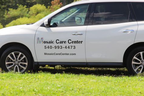 A close up of the drive side of a white SUV with Mosaic Care Center written on the side with their contact information, representing medical transportation, a sub service of HIV care offered by FAHASS.