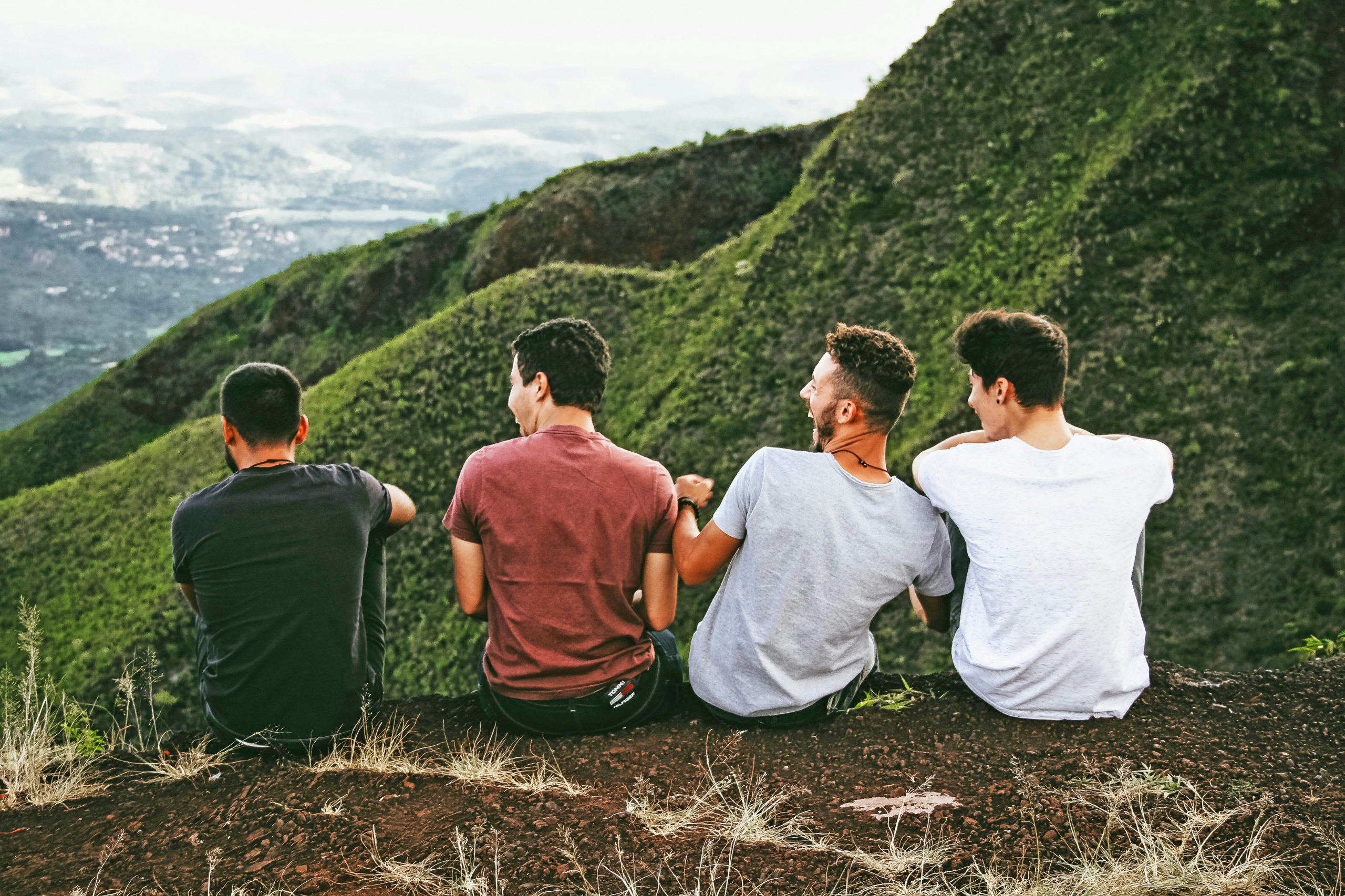 Four men sitting together on a scenic hill, laughing and sharing a moment of camaraderie, symbolizing the supportive community of the Gay & Bi Men's Group at Pride Center FXBG.