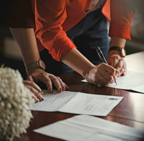 A close up of two people’s hands working on paperwork on a desk surface representing status neutral service navigation, a sub service of HIV care provided by FAHASS.