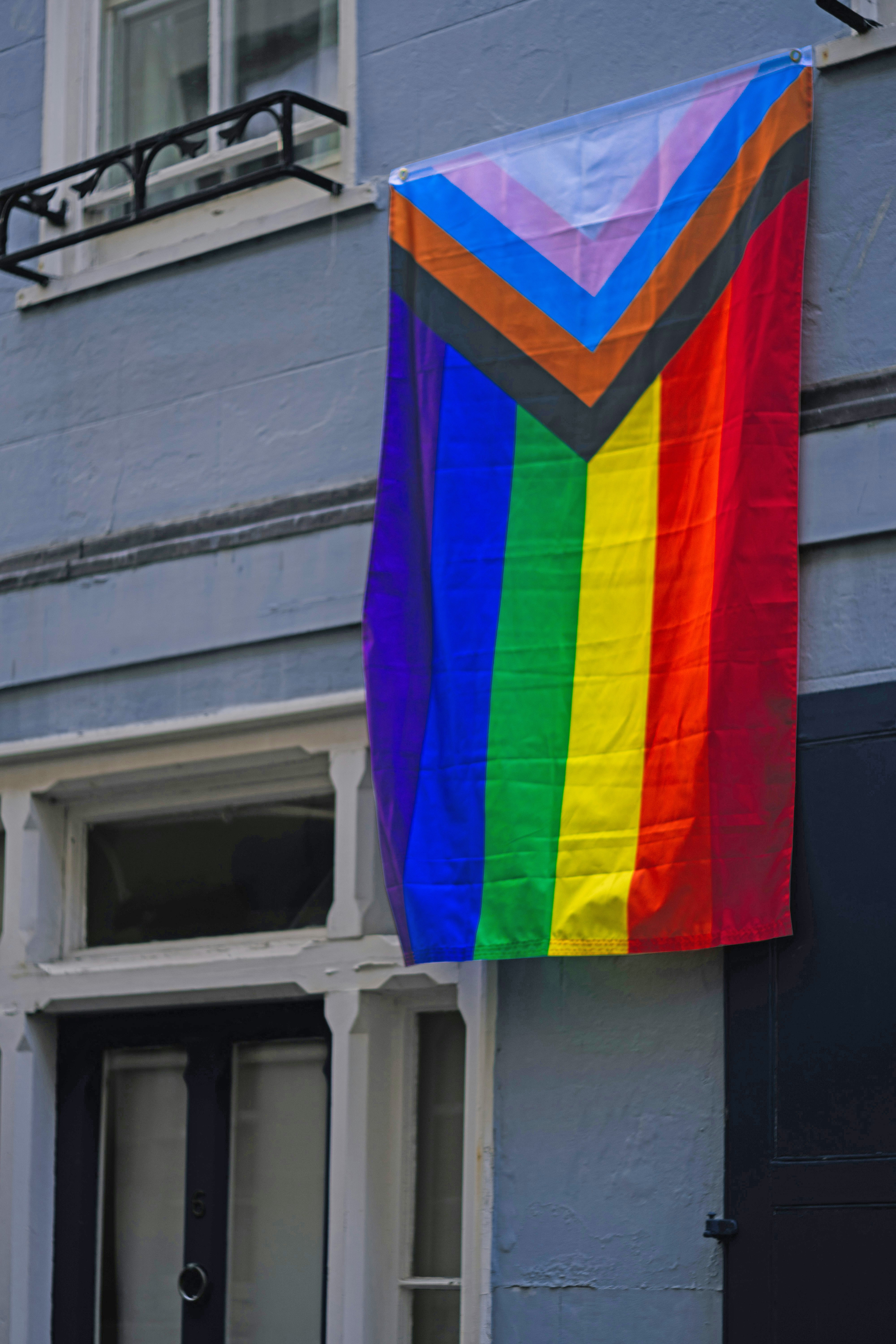 An LGBTQ+ pride flag hanging from a balcony representing LGBTQ+ support programs, a service offered by Pride Center FXBG, a division of FAHASS, in Fredericksburg, VA.