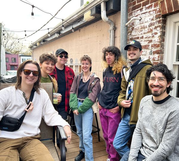 Lively gathering at the Queer Connection Coffee Social, hosted by FAHASS' Pride Center and Curitiba Art Cafe in Fredericksburg, VA, with diverse individuals on an outdoor patio.