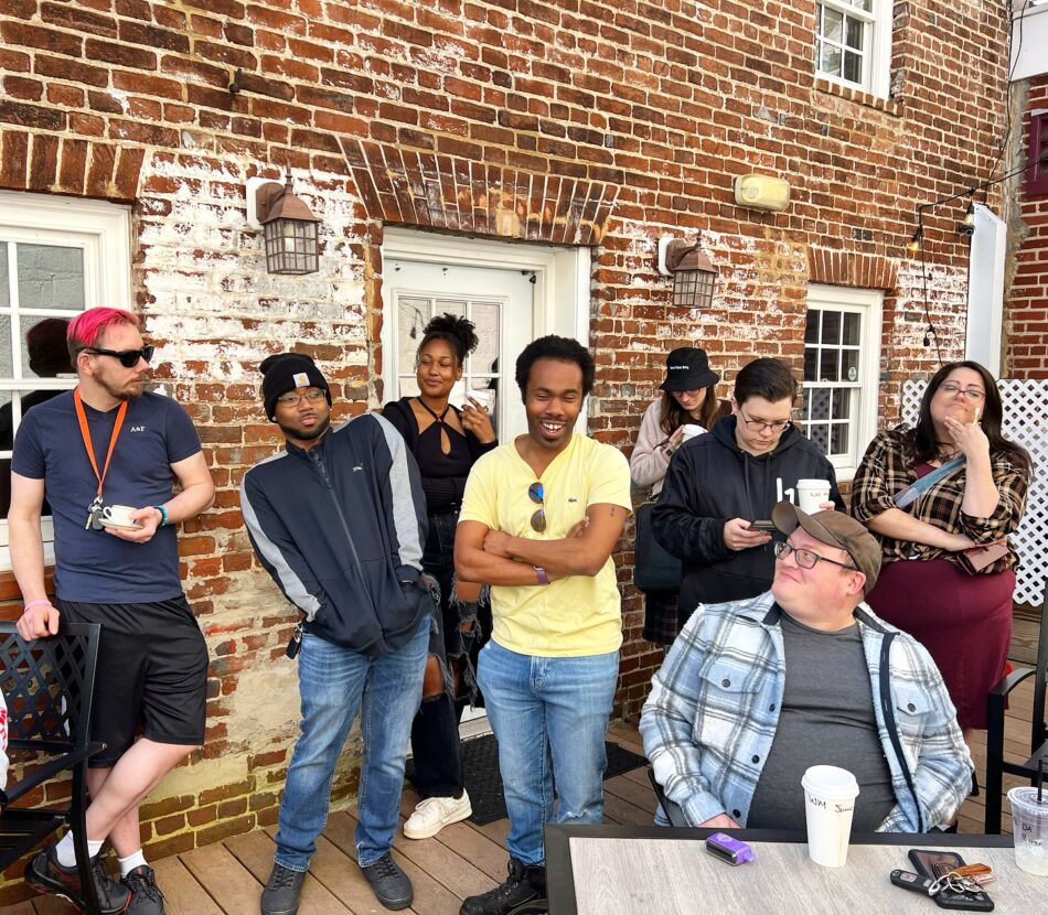 Lively gathering at the Queer Connection Coffee Social, hosted by FAHASS' Pride Center and Curitiba Art Cafe in Fredericksburg, VA, with diverse individuals on an outdoor patio.