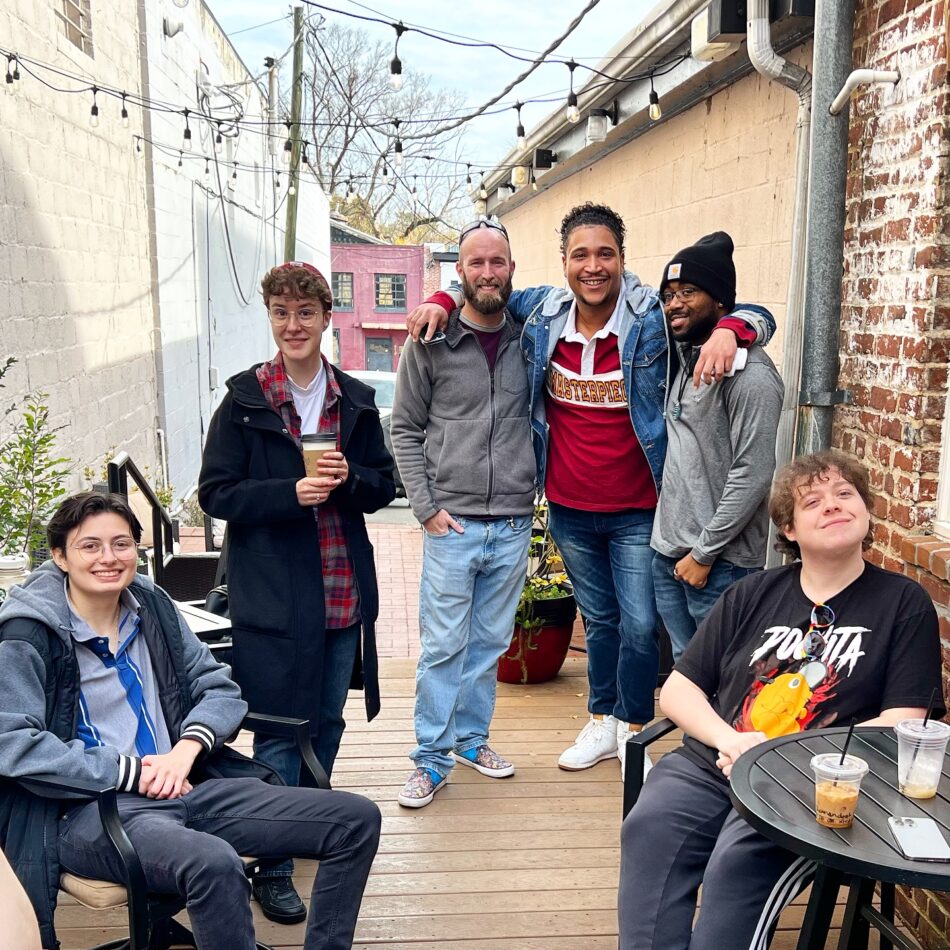 Lively gathering at the Queer Connection Coffee Social, hosted by FAHASS' Pride Center and Curitiba Art Cafe in Fredericksburg, VA, with diverse individuals on an outdoor patio.